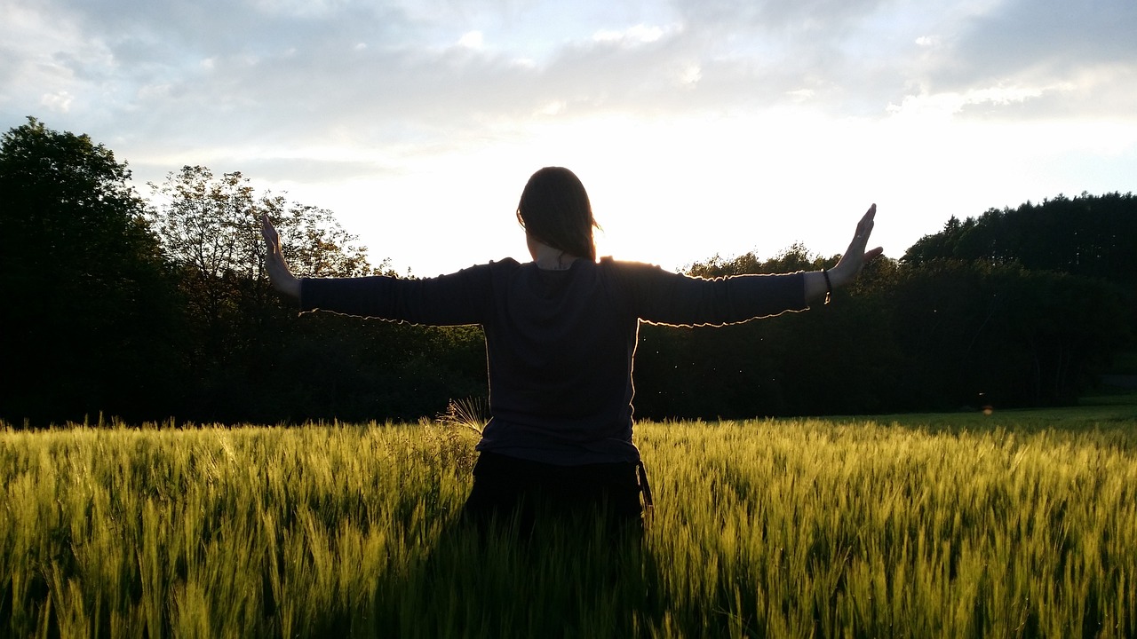 Frau steht mit ausgebreiteten Armen vor einem Feld in der Sonne